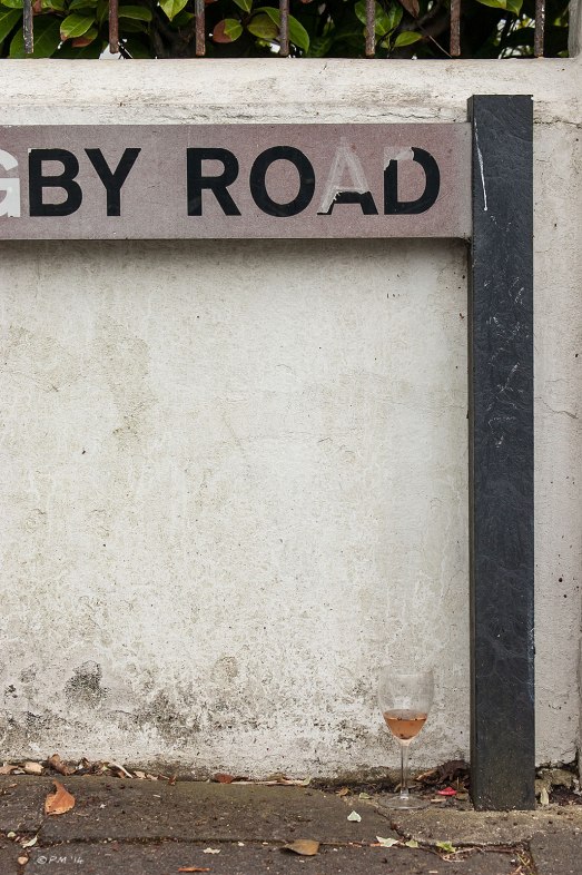 Abstract street name sign wall and wine glass on pavement  '...BY ROAD'