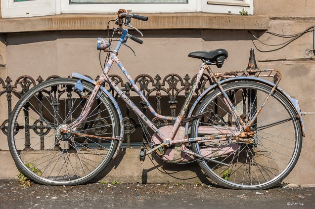 Old rusty bicycle with peeling pink and blue paint  and flat tyres leans against railings in front of house Brighton UK  29-4-2014 eyeteeth.net