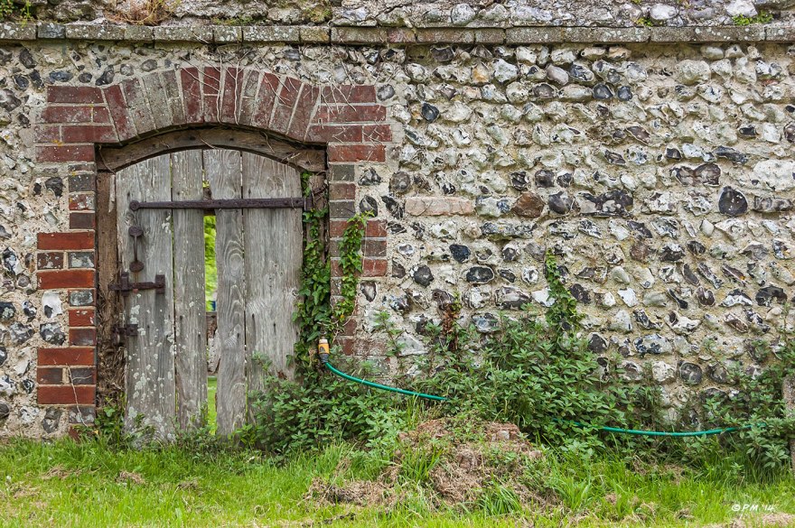 Knapped Flint Wall and small old wooded door leading to Glynde Place from St Mary's Church yard, water tap & hosepipe. Glynde Place East Sussex 2014 eyeteeth.net