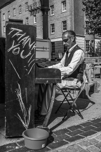 Man in shirt and waistcoat with eye patch and moustache playing piano in Trafalger Street Brighton UK monochrome busker P. Maton street photography 2014 eyeteeth.net