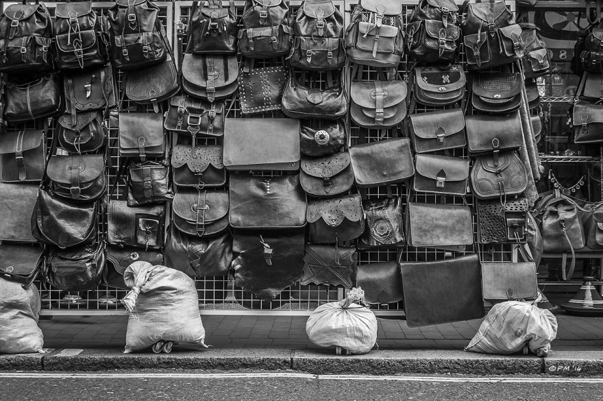 Wall of leather handbags and backpacks hanging on display outside a shop on Sydney Street, Brighton, UK. Monochrome. P.Maton 2014 eyeteeth.net