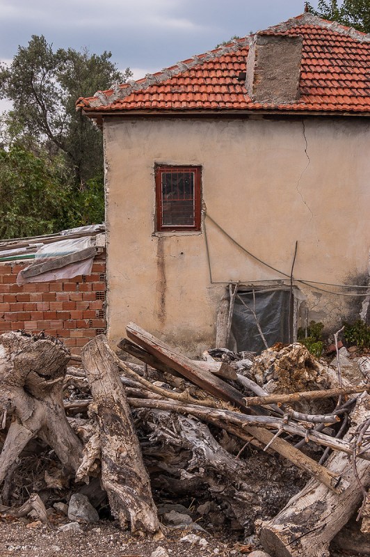 Side of dilapidated house with plastic covering doorway, log pile in foreground. Tlos, Turkey. Colour. P.Maton 2014 eyeteeth.net