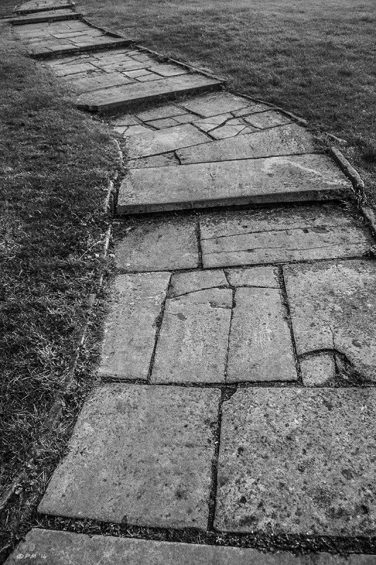Old flagstone path with steps snakes away from the camera through mown grass, St Nicholas Church Green Space, Brighton, East Sussex UK.. Monochrome abstract.  P.Maton 2014 eyeteeth.net