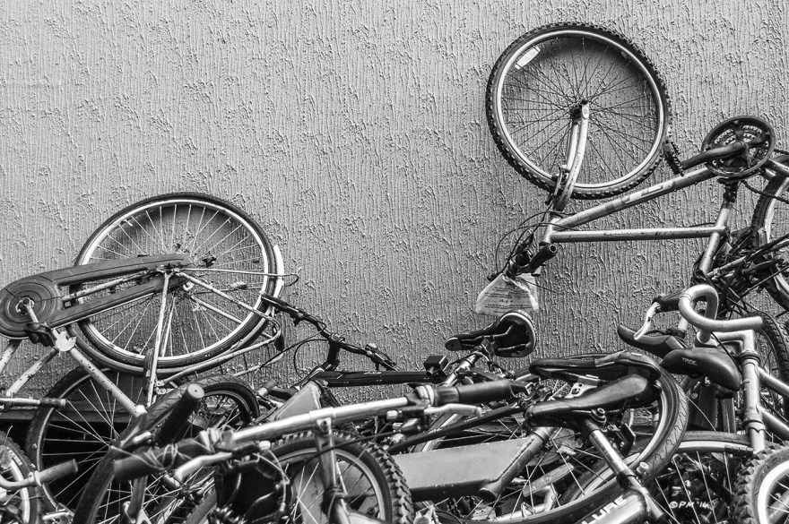 Broken bicycles piled against wall awaiting refurbishment. Monochrome landscape. © P. Maton 2014 eyeteeth.net