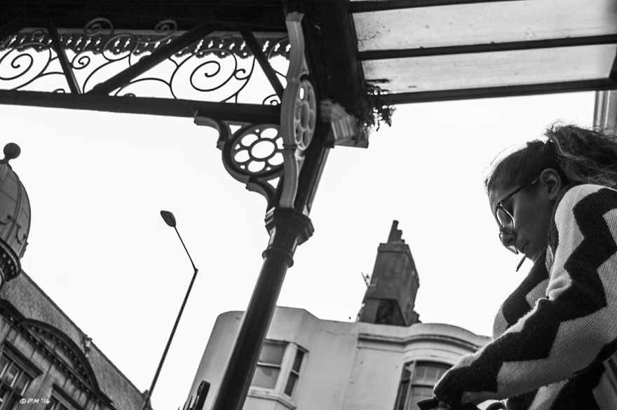 Woman smoking outside Brighton Railway Station with victorian roof and Grand Central Pub building in background. Monochrome landscape. © P. Maton 2014 eyeteeth.net