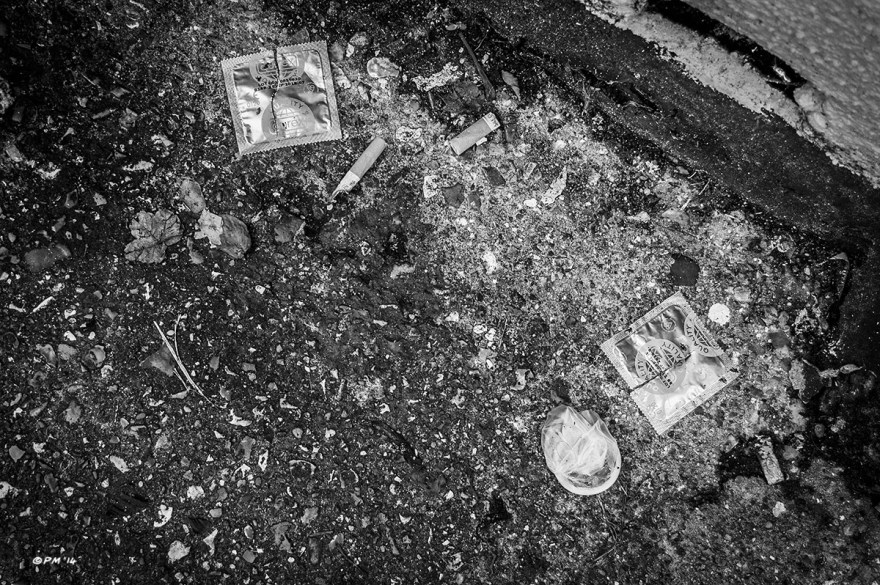 Torn condom wrappers and cigarette butts lying on tarmac in alley way, Brighton UK. Monochrome Landscape Abstract.  P. Maton 2014 eyeteeth.net