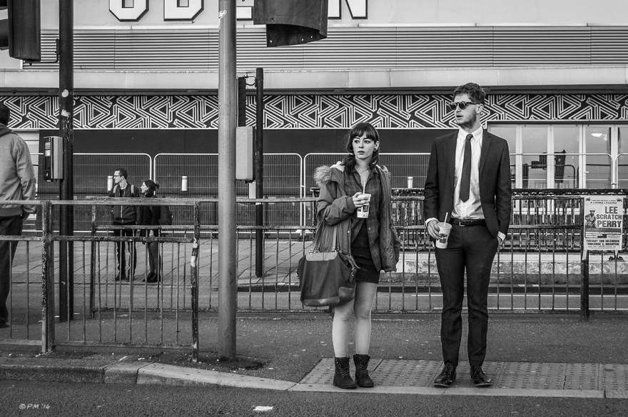 Young couple holding fast food drinks waiting at road crossing on Brighton seafront in front of Odeon Cinema, Brighton UK. Monochrome Landscape. © P. Maton 2014 eyeteeth.net