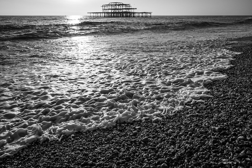 Ruins of West Pier and sunlight on sea with advancing water over shingle in foreground. Brighton UK. Monochrome Landscape. © P. Maton 2014 eyeteeth.net