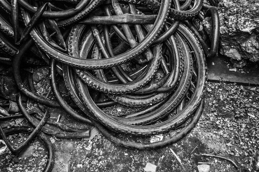 Bicycle theses piled up on muddy floor with detritus. Marion Road Hove UK. Monochrome Landscape Abstract. © P. Maton 2014 eyeteeth.net 