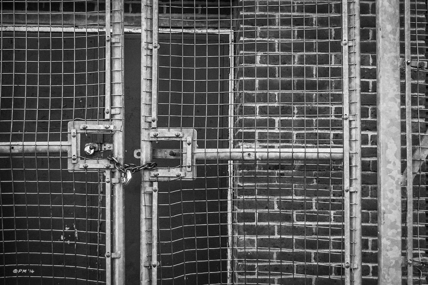 Padlocked metal gate in fence in fromt of locked door way in brick outbuilding, Playing field BHASVIC Brighton UK. Monochrome Landscape. © P. Maton 2014 eyeteeth.net