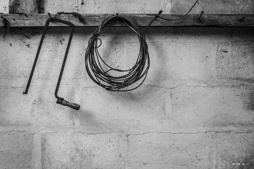 Coping saw and coiled cable hanging on beam in abandoned stable. Ford Lane, Frilford Oxfordshire UK. Monochrome Landscape. © P. Maton 2014 eyeteeth.net