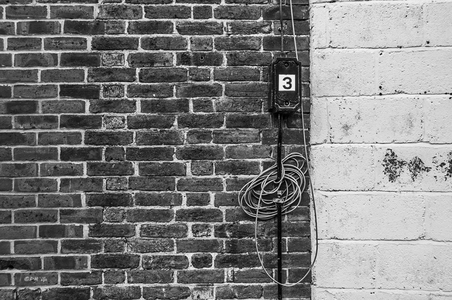 Metal electrical box with number three  and cable coil on brick wall next to white concrete block wall. Abstract. Lewes UK. Monochrome Landscape. © P. Maton 2015 eyeteeth.net