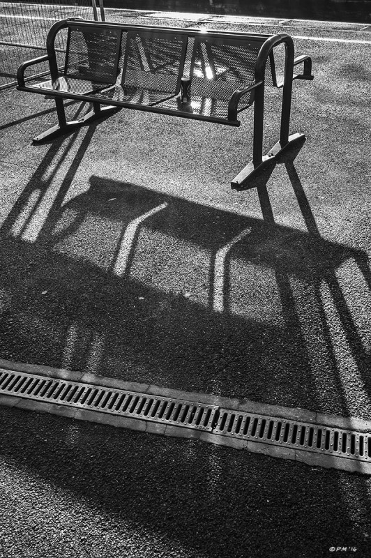 Metal bench with beer can casting long shadow towards viewer. Didcot Station, Oxfordshire UK. Monochrome  Portrait. © P. Maton 2014 eyeteeth.net