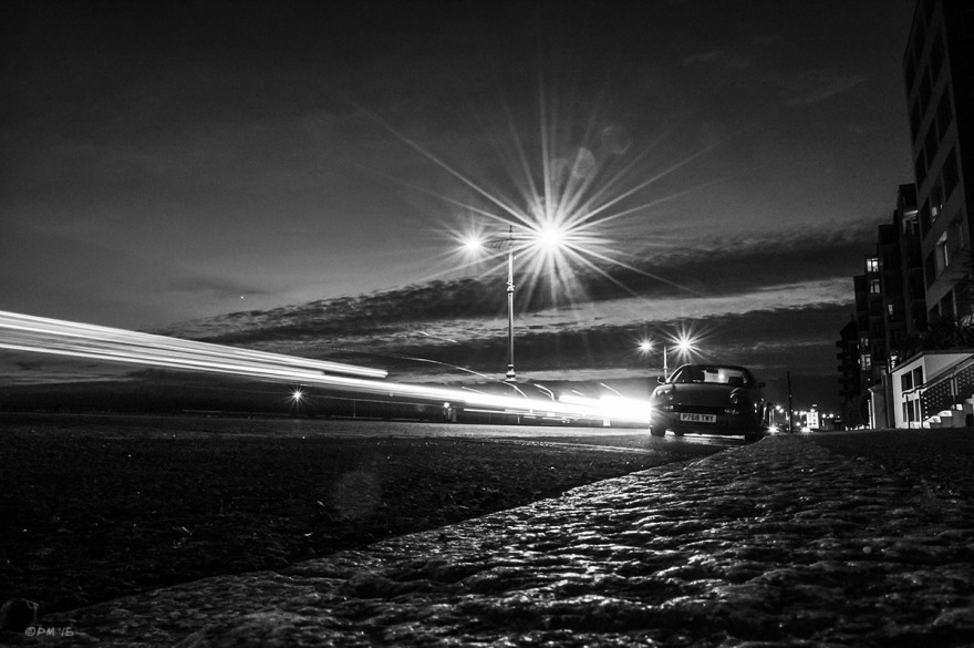 Streaks of light from passing cars with flare from street lamps , parked car and waining sunset. Kingsway Hove UK. Monochrome Landscape. © P. Maton 2015 eyeteeth.net