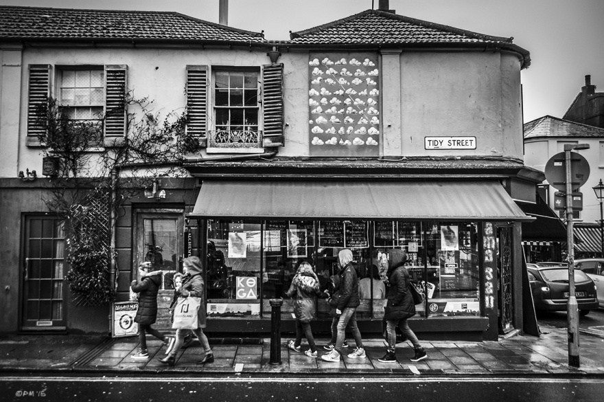 Young people walking under awning  of Mama San cafe in rain with cloud poster and windows above. Tidy Street North Laine Brighton UK. Monochrome Landscape. © P. Maton 2015 eyeteeth.net