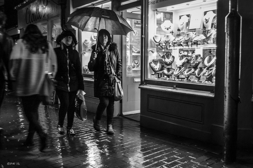 Mother and daughter with umbrella waling passed jewellers shop in rain at night. Kensington Gardens Brighton UK. Monochrome Landscape. © P. Maton 2015 eyeteeth.net