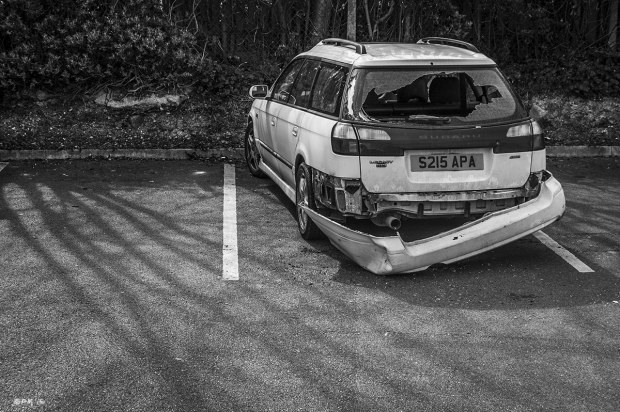 Subaru car with smashed back bumper and window in car park with shadows of trees on asphalt. Lewes, East Sussex UK.  Monochrome Landscape. © P. Maton 2015 eyeteeth.net