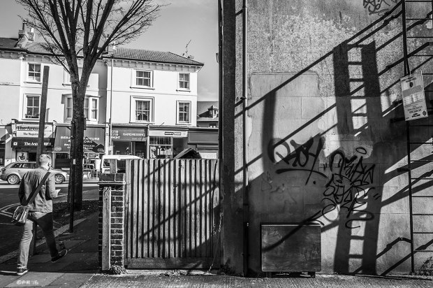 Shadows of fire escape ladder cast across side wall of building with man walking on pavement, Melville Rd with view on to Dyke Rd, Brighton UK. Monochrome Landscape. © P. Maton 2015 eyeteeth.net