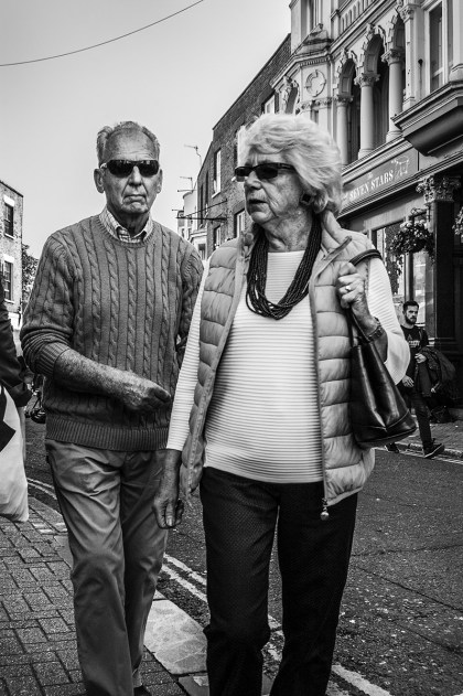 Senior couple in shades walking along street. Ship Street Brighton UK. Ship Street Brighton UK. Street Photography. Monochrome Portrait. © P. Maton 2015 eyeteeth.net