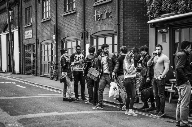 People gathered drinking and smoking outside The Eagle pub with man glancing down at young woman bottom as he leaves. Gloucester Road Brighton UK.Urban Street Photography. Monochrome Landscapet. © P. Maton 2015 eyeteeth.net 