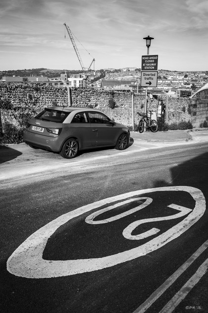 Road marking '20' in foreground with parked car and view across Brighton with diversion sign and crane. Howard Place, Brighton UK. Urban Street Photography.  Monochrome Portrait. © P. Maton 2015 eyeteeth.net