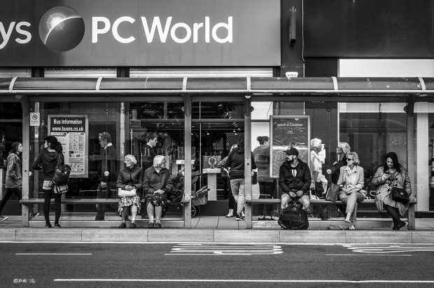 Two old women sisters sitting among people at bus stop in front of PC World, opposite Churchill Square, Western Road  Brighton UK. Monochrome Landscape. © P. Maton 2015 eyeteeth.net