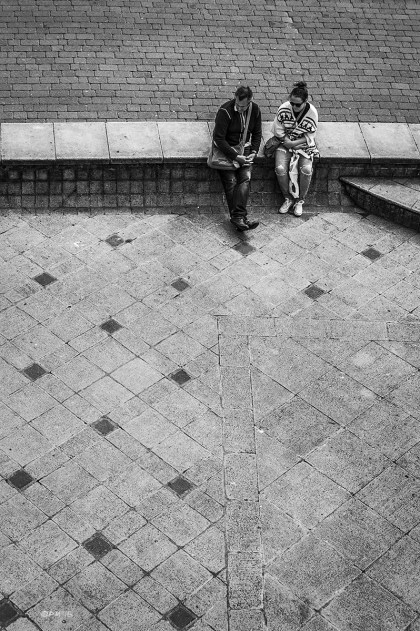 Man and woman couple sitting on wall between pathway and paved area seen from above. King's Road Arches Brighton UK. Monochrome Portrait. © P. Maton 2015 eyeteeth.net