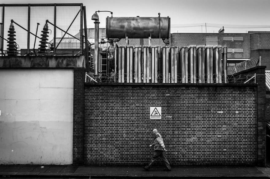 Man walking by brick wall with electrical substation above. Grim, bleak black and white British industrial urban street scene. Brighton UK © P. Maton 2015 eyeteeth.net