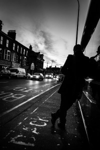 Silhouette of man leaning against bus stop shelter next to road with cars illuminating street and dawn light over Preston Circus, Brighton UK. Monochrome black and white urban street photography. © P. Maton 2016 eyeteeth.net