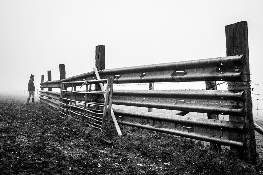 Farm armco fence by gate with woman standing in distance on foggy day. Fire Beacon, South Downs, Seven Sisters Country Park. East Sussex UK. Black and white landscape. © P. Maton 2016 eyeteeth.net