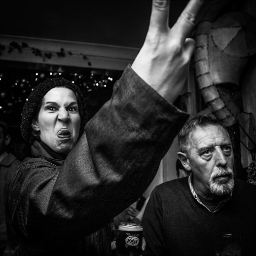 Woman in English pub pulling a face and sticking two fingers up at the camera while holding a pint of larger. Britain nightlife drinking culture. Shakespeare's Head pub Brighton. Black and white documentary photography. © P. Maton 2015 eyeteeth.net