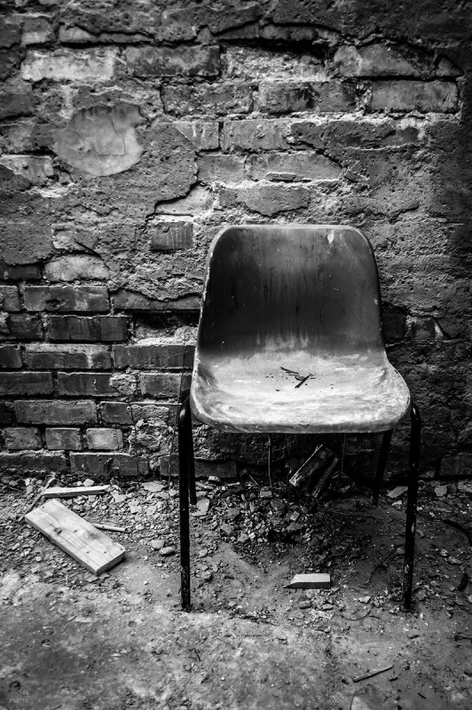 Dirty dusty plastic chair in front of crumbling plaster and brick wall with detritus on floor. Abandoned urban spaces photograph. Bexhill East Susex UK. © P. Maton 2016 eyeteeth.net