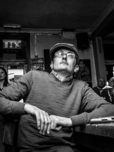Man in flat cap with glasses sitting staring upwards. Shakespeare's Heat Pub Brighton UK. Black and white nightlife photography. © P. Maton 2016 eyeteeth.net