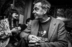 Man with rigged face and spiky hair in tweed jacket sitting at bar with people in background. Shakespeare's Head pub Brihjton UK. Black and white nightlife scene, character portrait, documentary © P. Maton 2016 eyeteeth.net