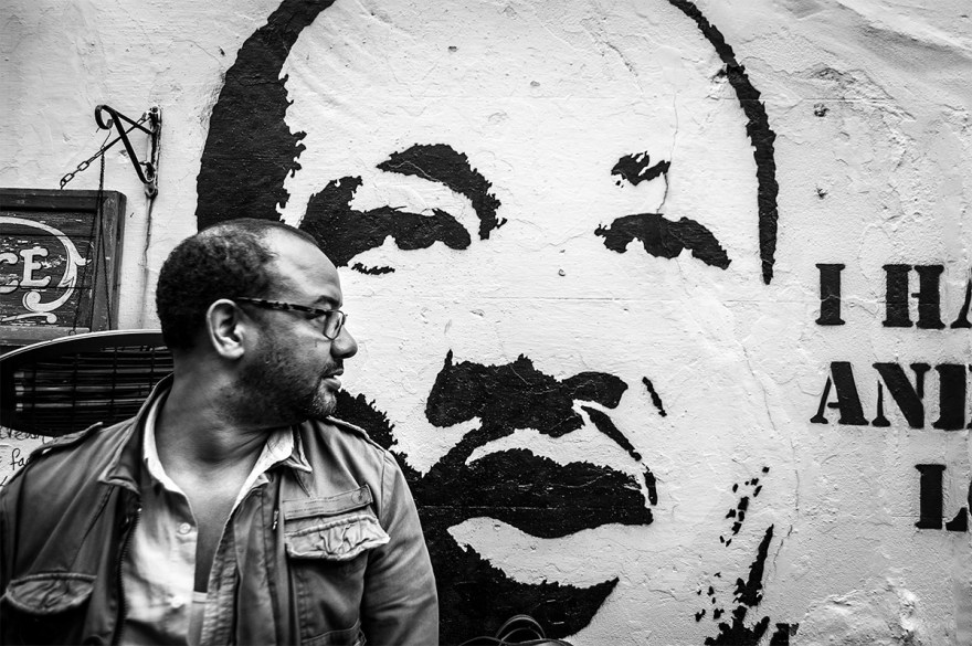 Man standing in front of wall street art stencil of Martin Luther King.  Black and white urban street documentary photography.  © P. Maton 2016 eyeteeth.net