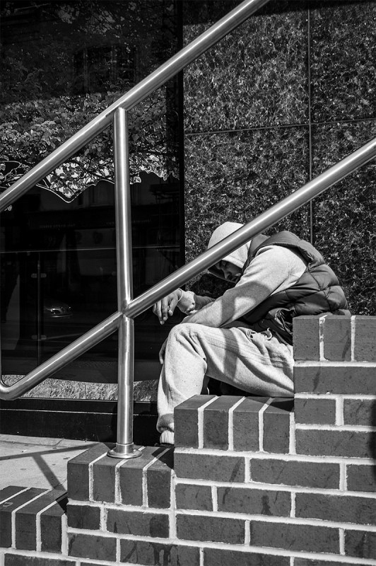 Drugged man with hoody over head possibly after taking Heroine sitting on steps nearly sleeping. Queens Road Brighton UK. Black and white urban street photography. © P. Maton 2016 eyeteeth.net