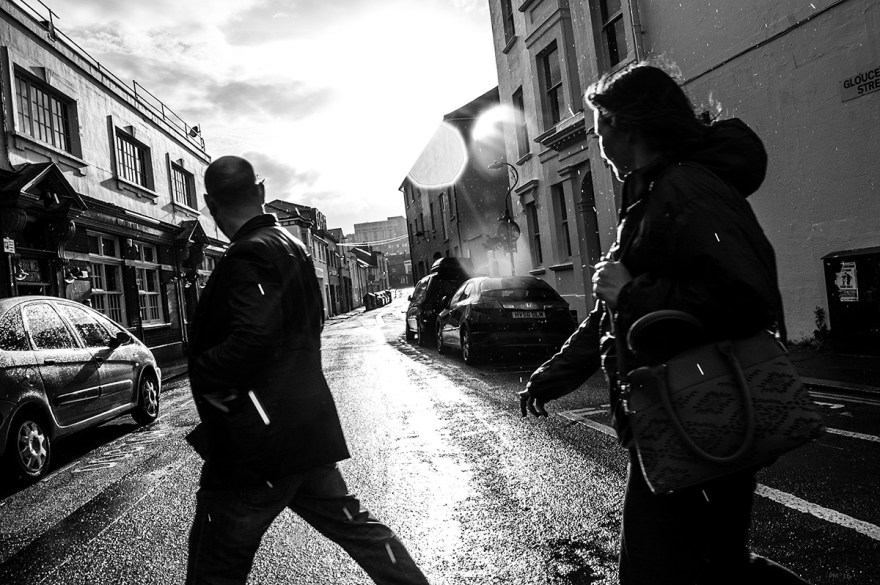 Silhouettes of people crossing wet road in sunshine and rain, Gloucester Street Brighton UK. Urban street photography black and white. © P. Maton 2016 eyeteeth.net
