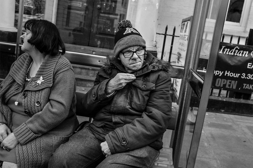 Couple sitting at bus stop with warm coats and wooly hat. North Street Brighton UK. Urban street photography. © P. Maton 2016 eyeteeth.net