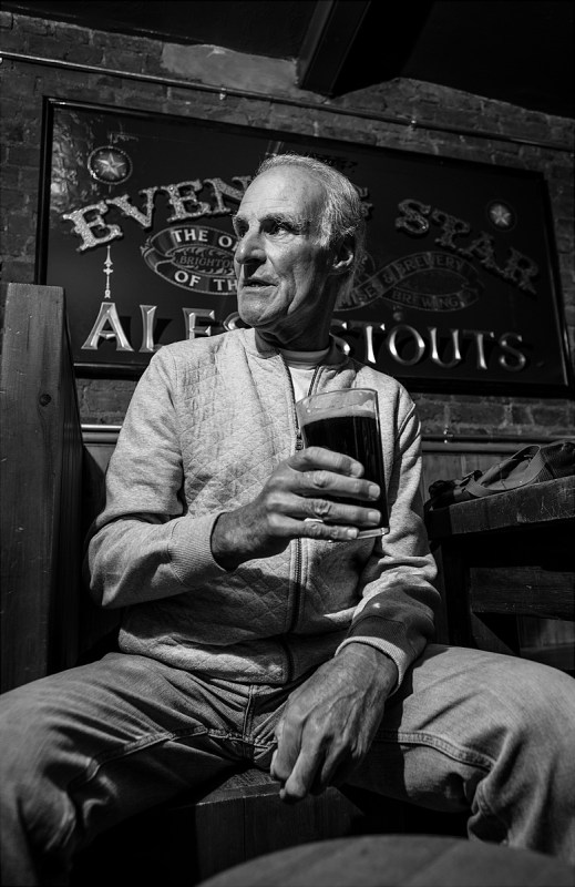 Man with pint of dark ale sitting in front of Evening Star pub sign. Brighton UK. Social documentary nightlife portrait black and white photograph. © P. Maton 2017 eyeteeth.net