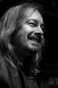 Candid portrait of a man with long hair a scruffy beard and a gold tooth wearing a leather jacket, Brighton UK black and white photograph © P. Maton 2017 eyeteeth.net