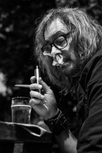 Man with long hair and glasses vaping while doing crossword and drinking a pint at a pub, Shakespeare's Head Chatham Place Brighton UK. Black and white nightlife portrait ©P. Maton 2017 eyeteeth.net