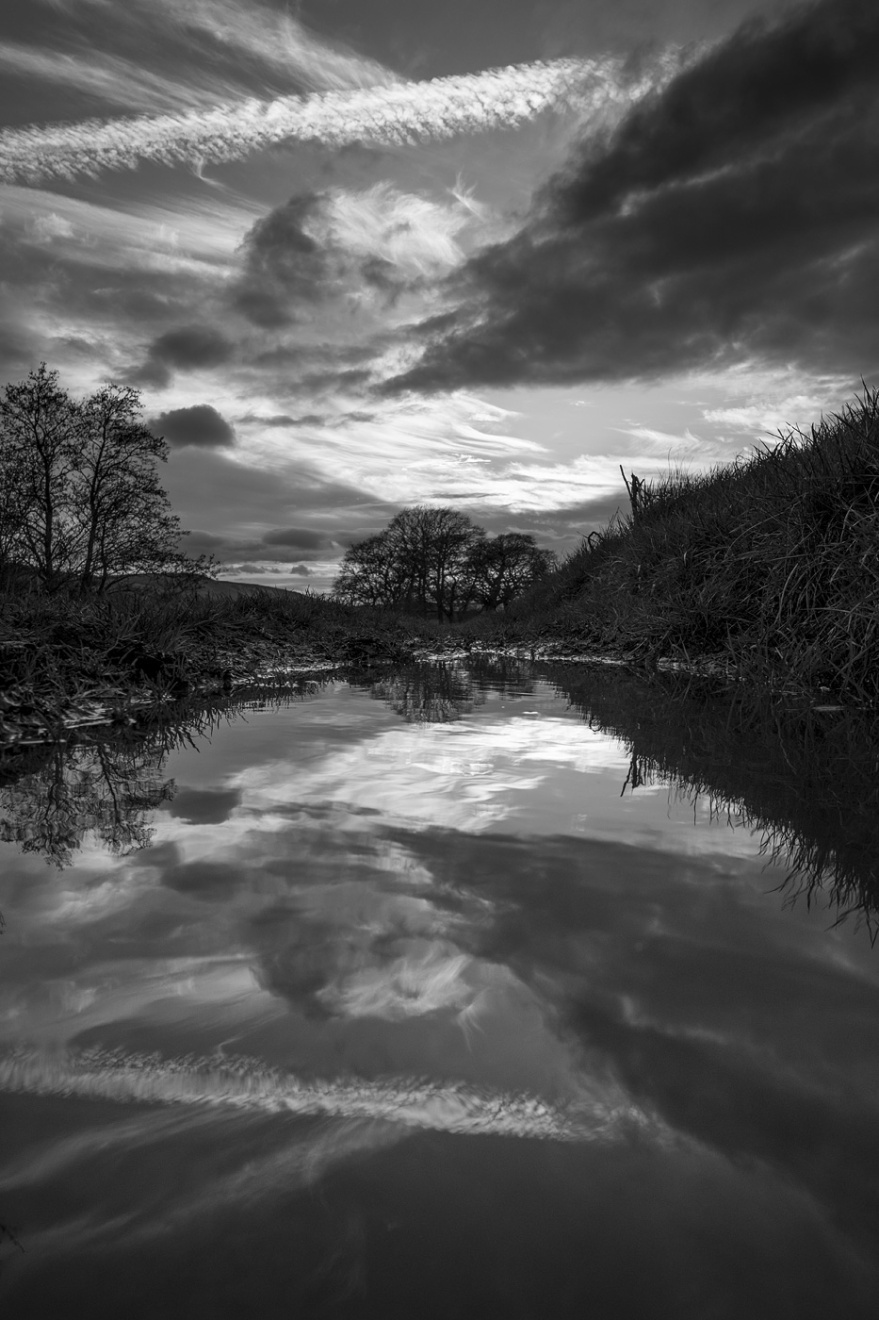 Dramatic clouds and contrail at sunset reflected in puddle, Mill Lane Poynings West Sussex UK black and white vertical portrait landscape rural countryside water photograph ©P. Maton 2018 eyeteeth.net