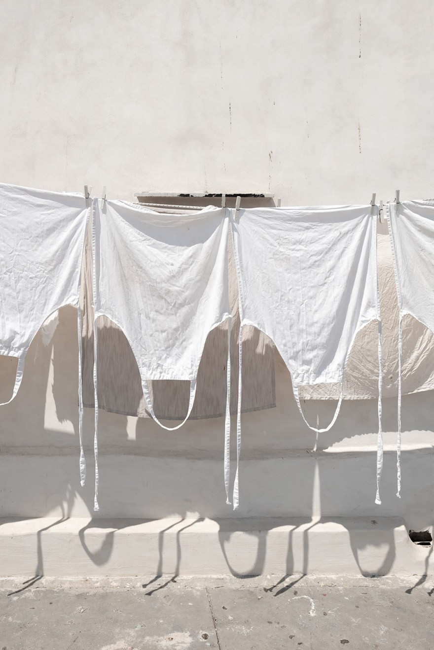 White aprons hanging out to dry in sunshine with whitewashed wall in background Via Marina di Corricella, Procida Italy abstract colour portrait composition urban street rustic photograph © P. Maton 2018 eyeteeth.net