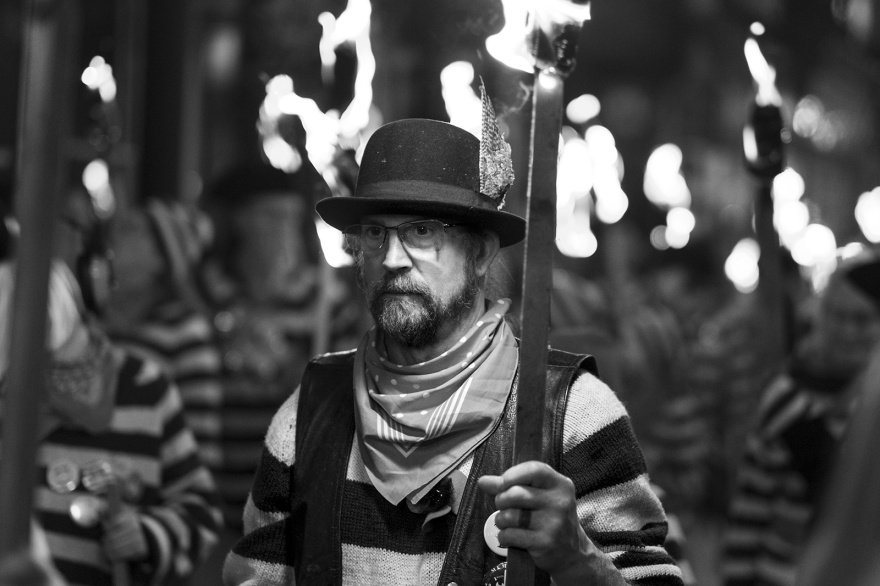 Male torch bearer in bowler hat and spectacles Lewes bonfire night Cliffe High Street Lewes East Sussex UK, black and white night photography Britain © P. Maton 2018 eyeteeth.net