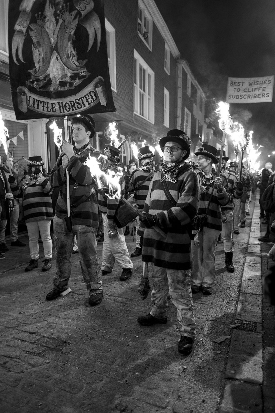 Little Horsted Male torch bearers in striped costume with burning standards Lewes bonfire night Cliffe High Street Lewes East Sussex UK, black and white night photography Britain © P. Maton 2018 eyeteeth.net