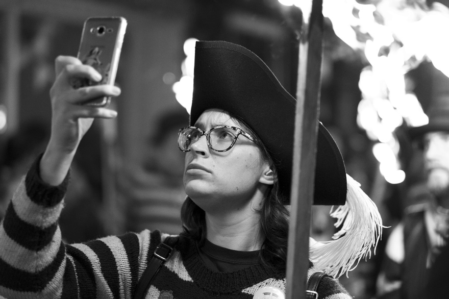 Female torch bearer in striped jersey and tricorn hat with phone and burning torches Lewes bonfire night Cliffe High Street Lewes East Sussex UK, black and white night photography Britain © P. Maton 2018 eyeteeth.net