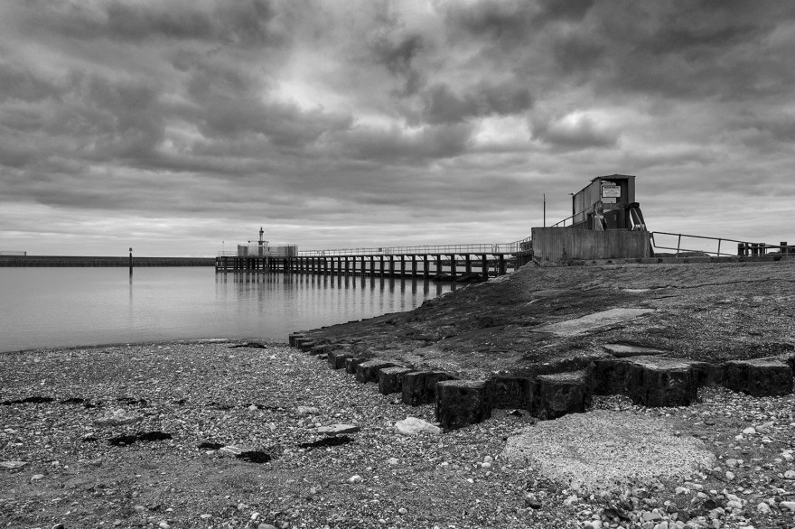 Shoreham harbour central pier with navigation beacon by entrance to eastern arm black and white landscape seascape with structures and overcast sky Shoreham by Sea West Sussex UK ©P. Maton 2019 eyeteeth.net